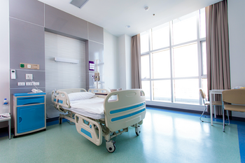 Ein verstellbares Krankenhausbett steht in einem hellen, sauberen Zimmer mit großen Fenstern.