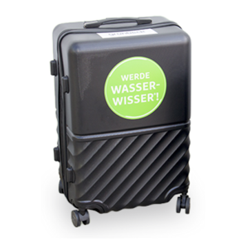 Ein schwarzer Koffer steht aufrecht mit einem grünen Aufkleber, auf dem "WERDE WASSERWISSER!" steht.