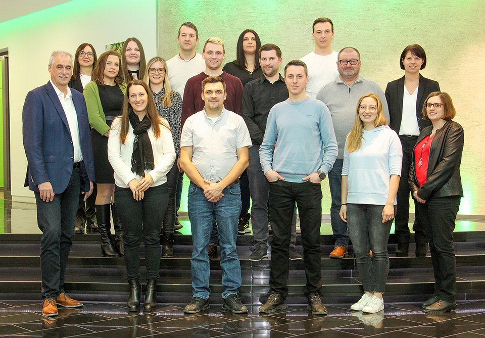 Eine Gruppe von Personen steht und lächelt in einem modern beleuchteten Raum auf schwarzen Stufen.