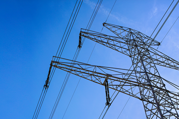Ein großes Strommast steht still gegen einen klaren blauen Himmel, umgeben von mehreren Stromleitungen.