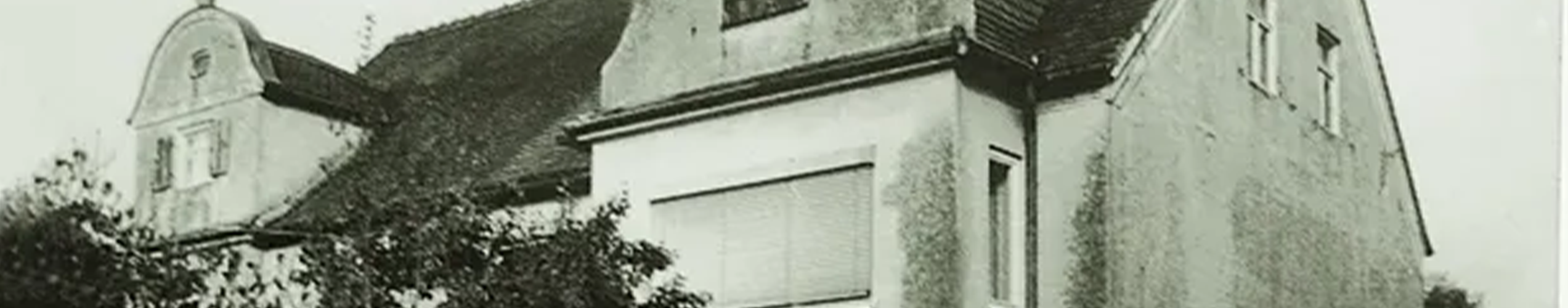 Schwarz-weiß Bild eines zweistöckigem, älterem Haus mit schrägem Dach.